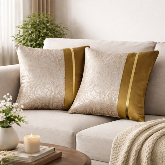 Two decorative throw pillows with a beige damask pattern and a vertical gold stripe, styled on a light beige sofa in a cozy living room setting.